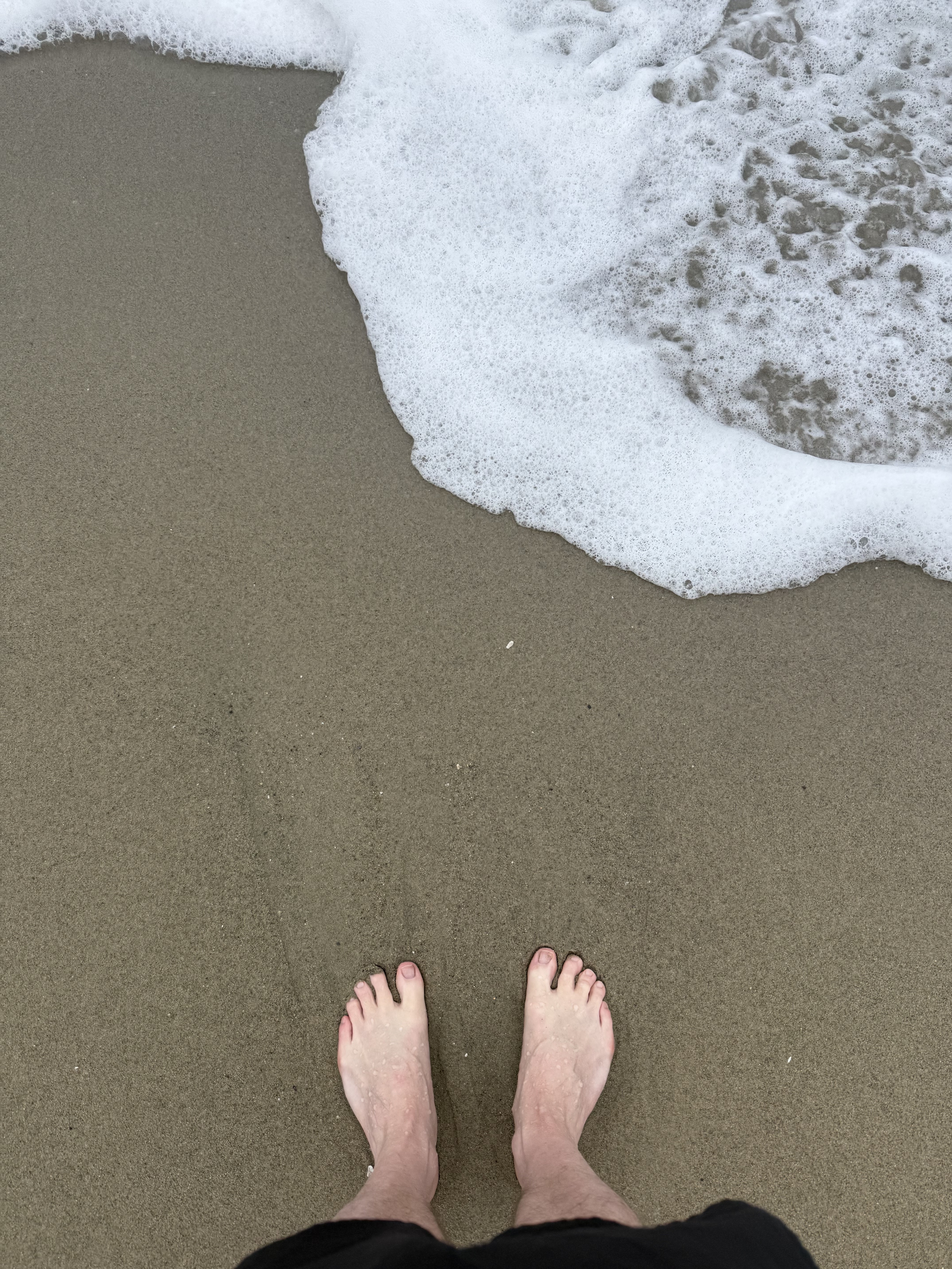Barefoot on wet sand, wave approaching