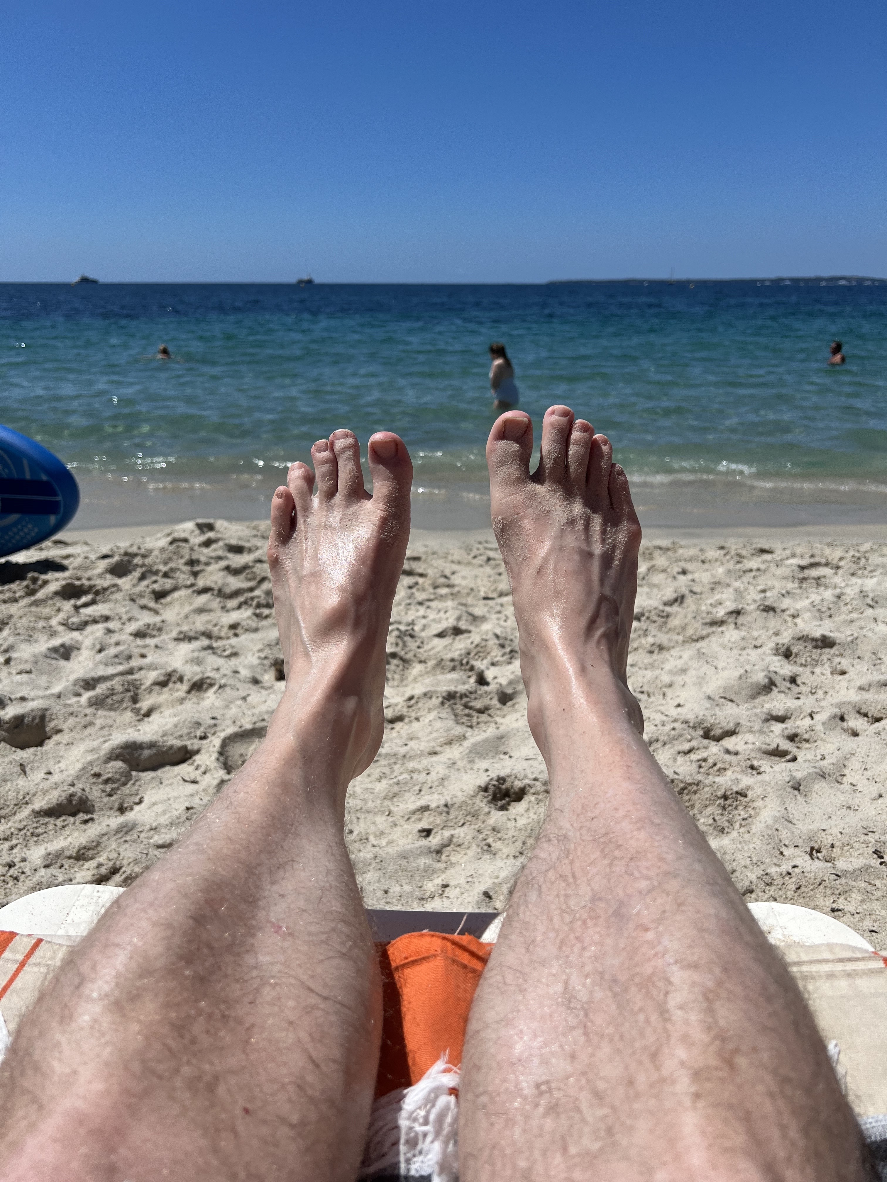 Feet up on sandy beach, blue sea beyond